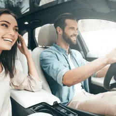 Un jeune homme souriant conduit, sa compagne à ses côtés, profitant de la **conduite supervisée accompagnateur**.