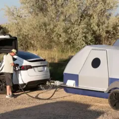 Homme chargeant une Tesla Model X blanche, prête à tracter une caravane de 750 kg.