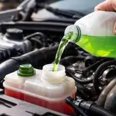 Main d'une personne versant du liquide de refroidissement vert dans le réservoir d'un moteur de voiture. Vérification de la consommation normale de liquide de refroidissement.