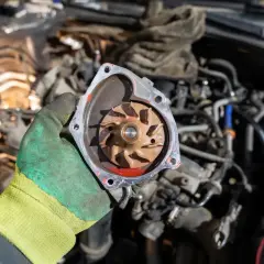 Main d'un mécanicien tenant une pompe à eau de voiture usagée, suggérant la fin de sa durée de vie.