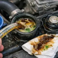 Une main verse un liquide brun dans le réservoir du liquide de refroidissement, où il se mélange à un liquide verdâtre. L'huile dans le liquide de refroidissement indique un problème.