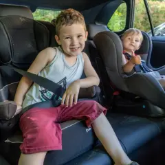 Deux enfants souriants dans leurs sièges auto, prêts pour le transport en voiture. Le plus grand fait un clin d'œil, le plus jeune montre son pouce levé.
