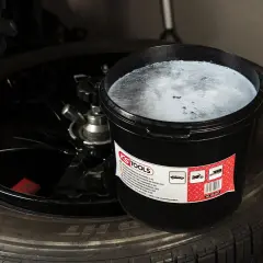 Un seau de pâte pour monter les pneus, vis dans pneu, est posé sur un pneu noir.