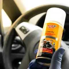 Main tenant de près une bombe aérosol pour le nettoyage climatisation voiture, devant un volant.