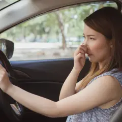 Une femme pince son nez, visiblement incommodée par l'odeur de climatisation voiture.