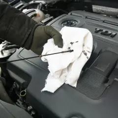 Main d'un mécanicien vérifiant le niveau d'huile avec une jauge. La jauge est sale, indiquant un problème avec la jauge huile moteur cassée.
