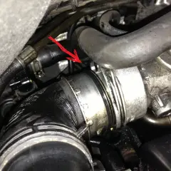 Flèche rouge pointe une durite turbo percée, suintant de l'huile dans le compartiment moteur.