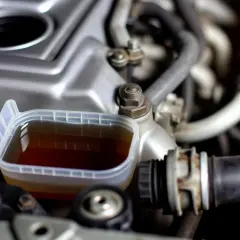 Un réservoir transparent contient du liquide de refroidissement marron, près du moteur d'une voiture.