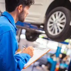 Mécanicien en bleu notant les détails sur un ordre de réparation voiture, avec un véhicule sur un pont élévateur.