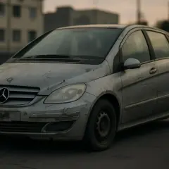 Mercedes Classe B, un modèle à éviter, sale et abîmé, stationné devant des bâtiments délabrés.