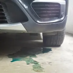 Une flaque de liquide de refroidissement couleur turquoise s'étend sous le pare-chocs d'une voiture garée.