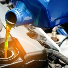 Un bidon bleu verse un liquide de transmission jaune vif dans le moteur d'une voiture.