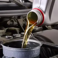 Huile moteur versée dans un entonnoir, étape clé avant la vidange par aspiration. Le moteur de la voiture est visible en arrière-plan.