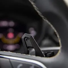 Gros plan sur une palette au volant, prête pour un changement de vitesse sportif. Le tableau de bord flou en arrière-plan suggère une conduite dynamique.