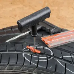 Kit de réparation pour pneu de voiture : un outil insère une mèche dans un pneu crevé, prêt à réparer.