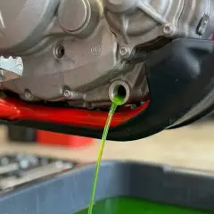 Vidange du liquide de refroidissement OAT d'une moto. Le liquide vert vif s'écoule du moteur dans un bac de récupération.