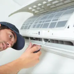 Un technicien répare une climatisation bruyante. Il utilise un tournevis pour ajuster une pièce.