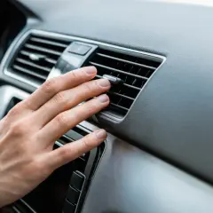 Main d'une personne ajustant la direction de l'air d'une grille de ventilation de voiture, près d'un bouton clim voiture.