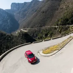 Voiture rouge sur route de montagne sinueuse. Le frein moteur de la boîte automatique gère la descente.