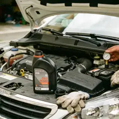 Vidange Peugeot 208 : une bouteille d'huile moteur et des gants sont posés sur le capot ouvert. Un manomètre est connecté à la batterie.