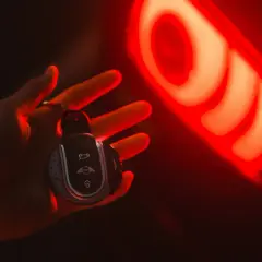 Clé de voiture Mini dans une main, éclairée par le feu arrière rouge. Une image qui évoque la recherche du prix moyen voiture occasion.