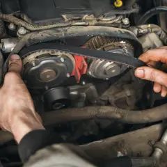 Mains d'un mécanicien ajustant la courroie de distribution essence sur un moteur de voiture.