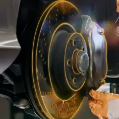Inspection d'un frein de service de voiture. Un mécanicien utilise une lampe torche pour examiner le disque et l'étrier.
