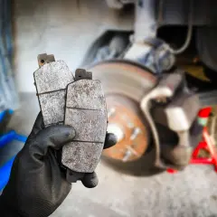 Main tenant deux plaquettes de frein usées, prêtes pour un remplacement. La graisse pour plaquette de frein est essentielle pour un bon fonctionnement.