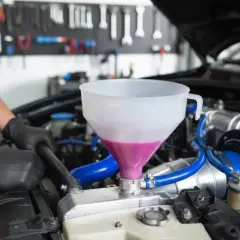 Maintenant, comment purger le liquide de refroidissement sans vis de purge. Un mécanicien verse du liquide rose dans un entonnoir connecté au radiateur.