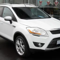Un Ford Kuga blanc, symbole de fiabilité, garé devant un showroom.