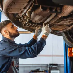 Mécanicien inspectant le dessous d'une voiture, cherchant la cause d'un embrayage bloqué en bas.