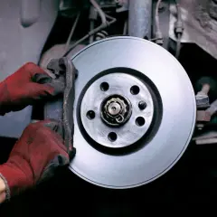 Mains gantées en rouge travaillent sur le disque de frein pour changer la plaquette.