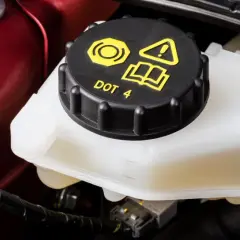 Réservoir de liquide de frein DOT 4, le niveau est visible sur le côté du récipient blanc.