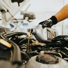 Main d'un mécanicien versant de l'huile neuve dans le moteur d'une voiture diesel. L'entretien régulier est essentiel pour la vidange de votre voiture diesel.