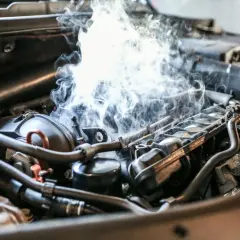 Fumée épaisse s'échappe d'un moteur de voiture, suggérant un bruit de cliquetis moteur diesel inquiétant.