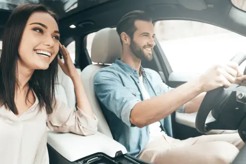 Un jeune homme souriant conduit, sa compagne à ses côtés, profitant de la **conduite supervisée accompagnateur**.