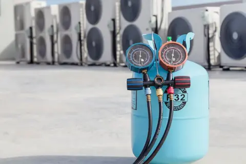 Bouteille de gaz R32 pour climatisation de voiture, avec manomètres, devant des unités extérieures de climatisation.