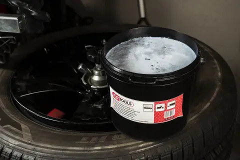 Un seau de pâte pour monter les pneus, vis dans pneu, est posé sur un pneu noir.