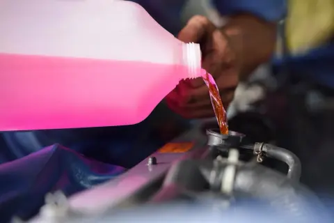Main d'un mécanicien versant du liquide de refroidissement rose dans le radiateur d'une voiture. C'est le moment idéal pour savoir quand changer liquide de refroidissement.