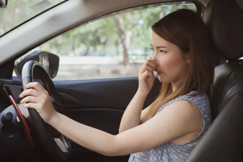Une femme pince son nez, visiblement incommodée par l'odeur de climatisation voiture.