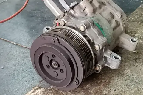 Compresseur de climatisation automobile, prêt pour son remplacement. Pièce mécanique essentielle pour le confort de conduite.