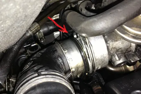 Flèche rouge pointe une durite turbo percée, suintant de l'huile dans le compartiment moteur.