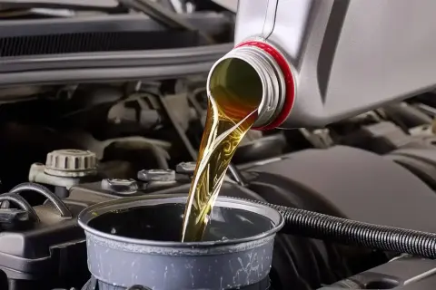 Huile moteur versée dans un entonnoir, étape clé avant la vidange par aspiration. Le moteur de la voiture est visible en arrière-plan.