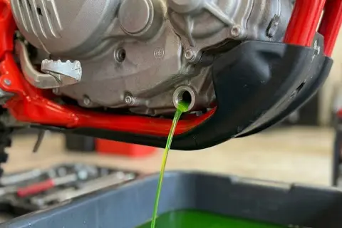 Vidange du liquide de refroidissement OAT d'une moto. Le liquide vert vif s'écoule du moteur dans un bac de récupération.