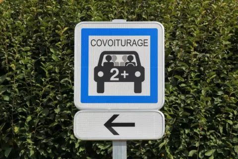 Panneau de signalisation "Covoiturage" indiquant une voie réservée aux véhicules de 2 personnes ou plus. Une flèche noire pointe vers la gauche.