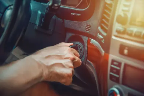 Main d'un conducteur tournant la clé de contact, espérant que la voiture cale en roulant ne se reproduise pas.