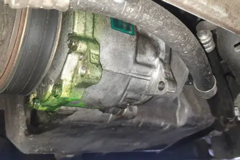 Recherche fuite clim auto : le compresseur est couvert d'un liquide vert fluorescent, signe d'une fuite.