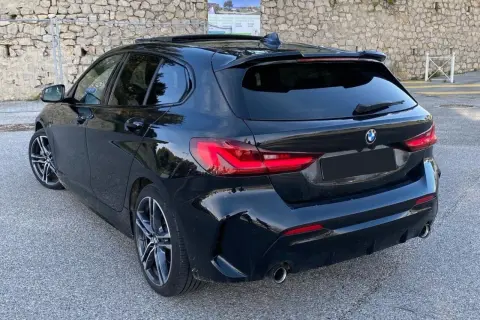 Vue arrière d'une BMW Série 1 F40 noire, un modèle à éviter pour certains. Jantes sport, spoiler, toit ouvrant.