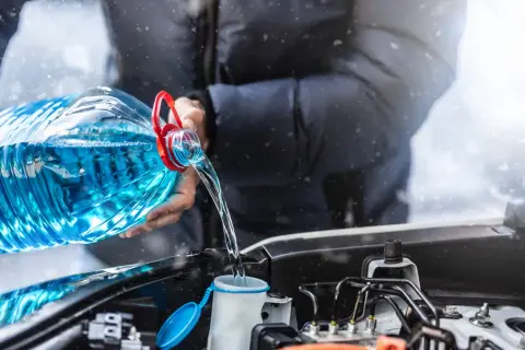 Person verse une grande bouteille de lave glace maison dans le réservoir de la voiture, sous une légère chute de neige.