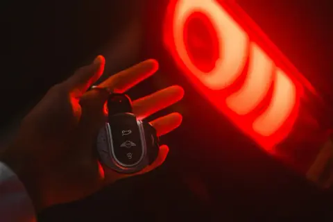 Clé de voiture Mini dans une main, éclairée par le feu arrière rouge. Une image qui évoque la recherche du prix moyen voiture occasion.